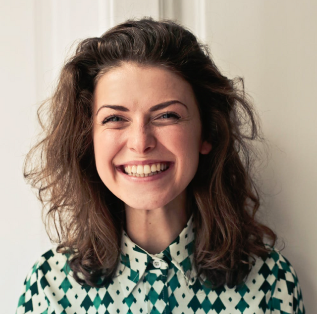 A girl wearing a green patterned blouse looking fresh-faced and smiling.