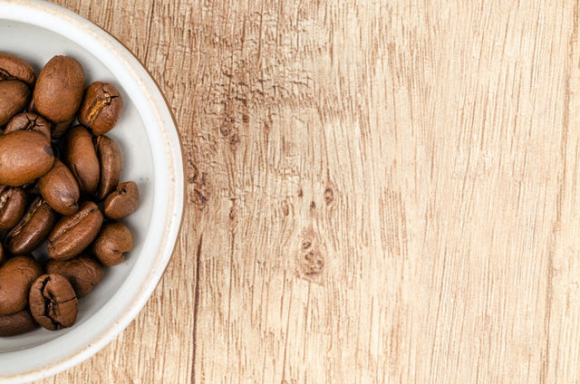 Coffee beans in a white cup on a wooden table.