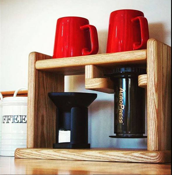 An AeroPress on wooden shelving with red mugs
