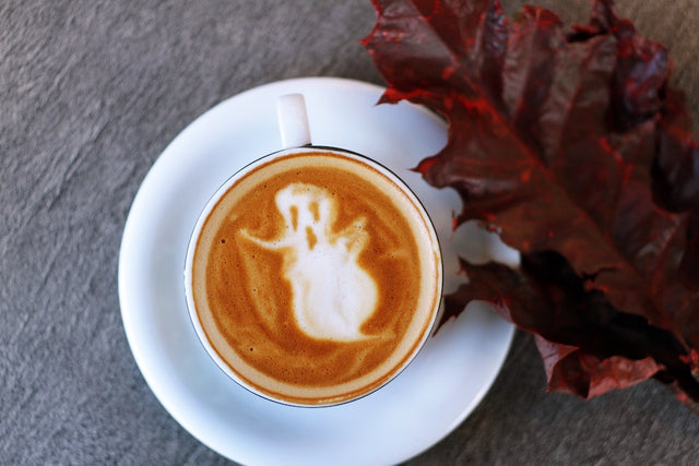 A coffee with ghost latte art next to a red leaf