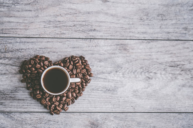 cup of coffee sat on a heart made of coffee beans